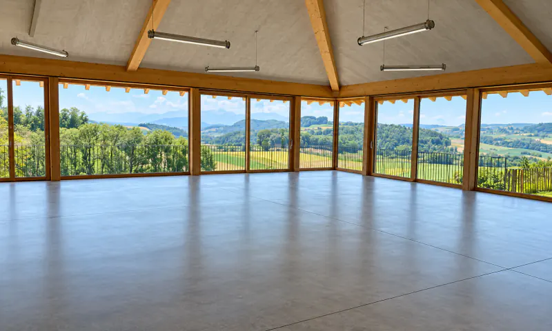 Salle villageoise lumineuse avec baies vitrées donnant sur la campagne